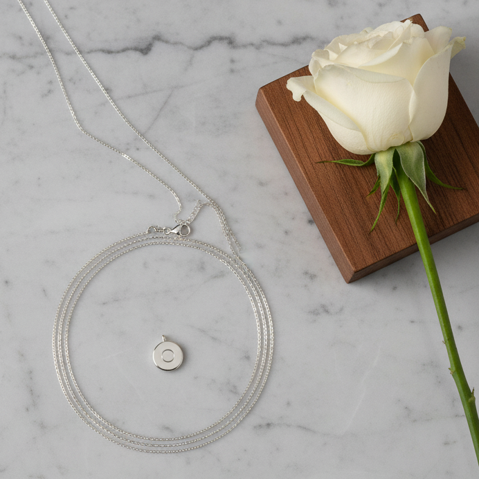 Silver Safetrack Aura Necklace on a marble surface next to a white rose.